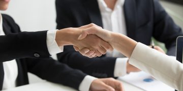 two people shaking hands in front of a laptop