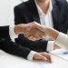 two people shaking hands in front of a laptop