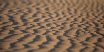 Close-up of rippled sand patterns in the desert during sunset, highlighting natural textures.