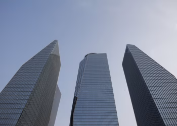 Three tall modern skyscrapers rise dramatically against a clear blue sky.