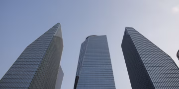 Three tall modern skyscrapers rise dramatically against a clear blue sky.