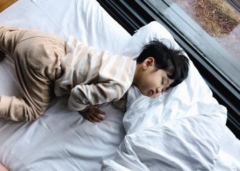 An Asian child peacefully sleeping in cozy pajamas by a window, indoors.