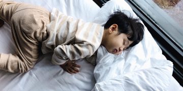 An Asian child peacefully sleeping in cozy pajamas by a window, indoors.