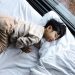 An Asian child peacefully sleeping in cozy pajamas by a window, indoors.