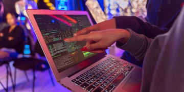 A vibrant scene with hands pointing at a computer with code on display, suggesting tech focus.