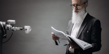 A robot arm assists a professional with a book and coffee in a modern office setup. Technology meets innovation.