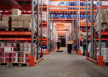 Warehouse interior showing workers handling boxes and organized shelves filled with products.