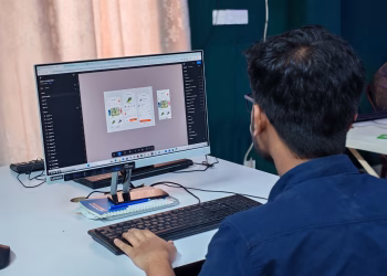 A young designer focused on creating user interfaces on a desktop computer in an office setting.