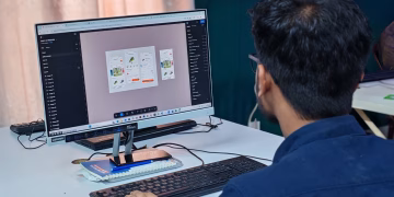 A young designer focused on creating user interfaces on a desktop computer in an office setting.