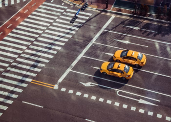 Two yellow taxis navigate a city intersection with marked pedestrian crossings.
