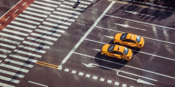 Two yellow taxis navigate a city intersection with marked pedestrian crossings.