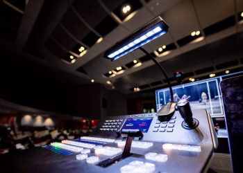 Contemporary music console with buttons and glowing lamp under ceiling with lights in dark studio