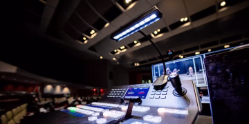 Contemporary music console with buttons and glowing lamp under ceiling with lights in dark studio