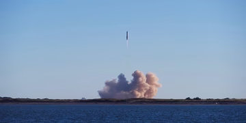 A rocket launch with smoke trails over South Padre Island, viewed across the ocean.