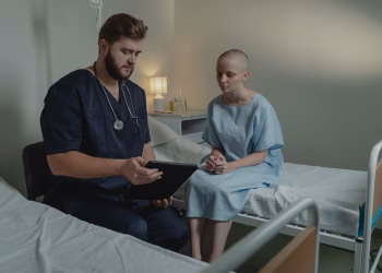 A doctor in a hospital ward consulting a patient with a digital tablet.