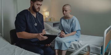 A doctor in a hospital ward consulting a patient with a digital tablet.