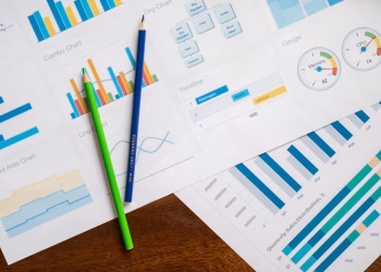 Flat lay of various business charts and colored pencils on wooden table, highlighting financial analysis.