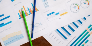 Flat lay of various business charts and colored pencils on wooden table, highlighting financial analysis.