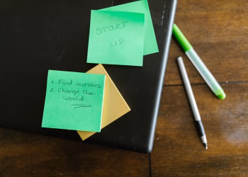 Green sticky notes with startup goals on a wooden desk with pens.
