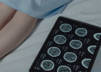 Close-up of brain CT scan display on tablet beside patient's legs in a hospital room.