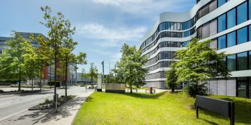 Contemporary business office building with curved architecture and trees in an urban setting.