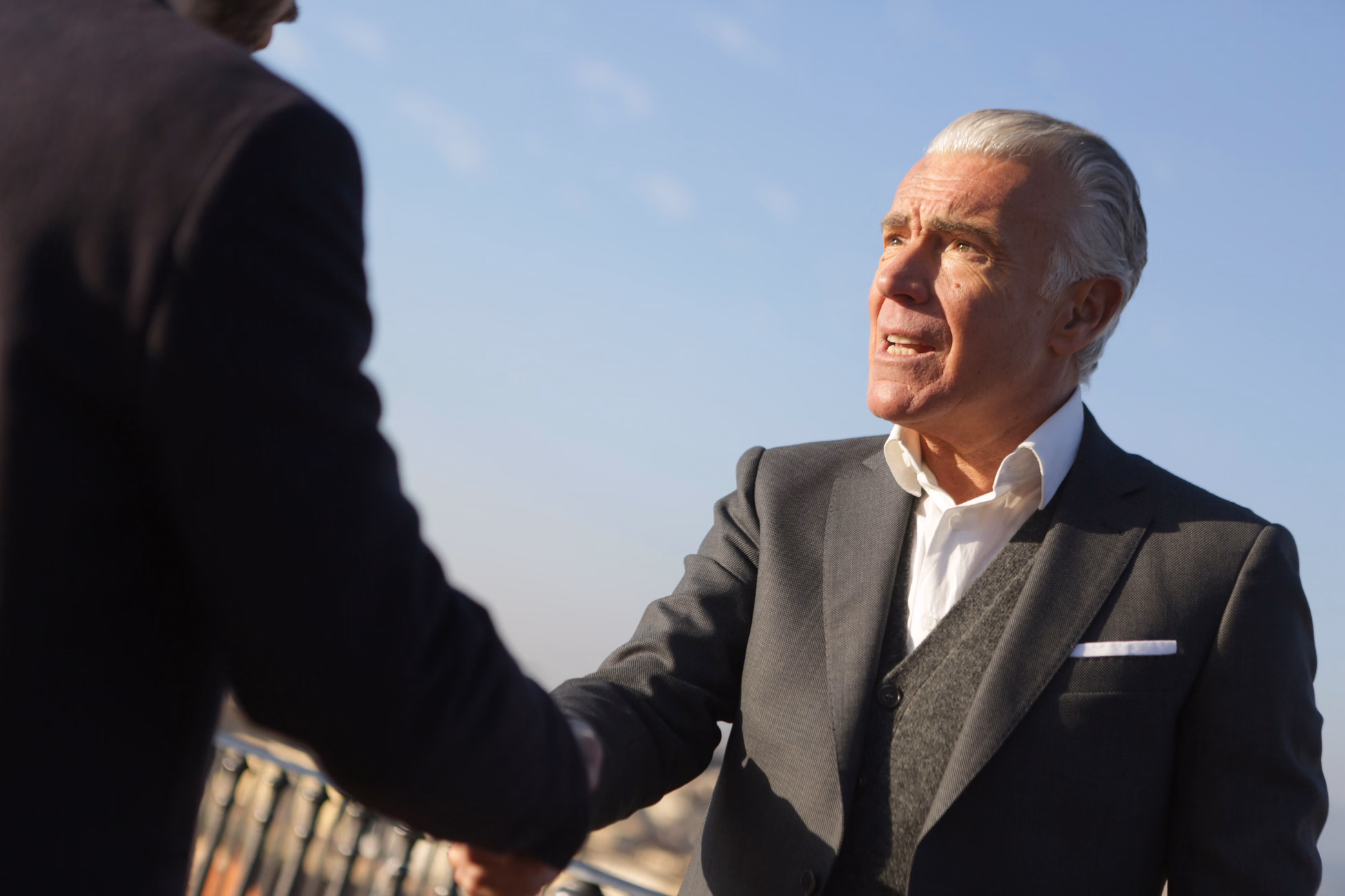 From below of serious male chief director in classy wear standing on street and shaking hands with business partner while reaching agreement and looking at each other