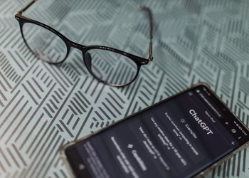Eyeglasses next to a smartphone displaying the ChatGPT AI app on a patterned surface.