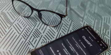 Eyeglasses next to a smartphone displaying the ChatGPT AI app on a patterned surface.
