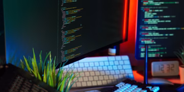 A vibrant workspace showing computer monitors with code, keyboard, and tech accessories.