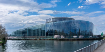 Modern architecture of the European Parliament building in Strasbourg with a reflective glass facade and river view.