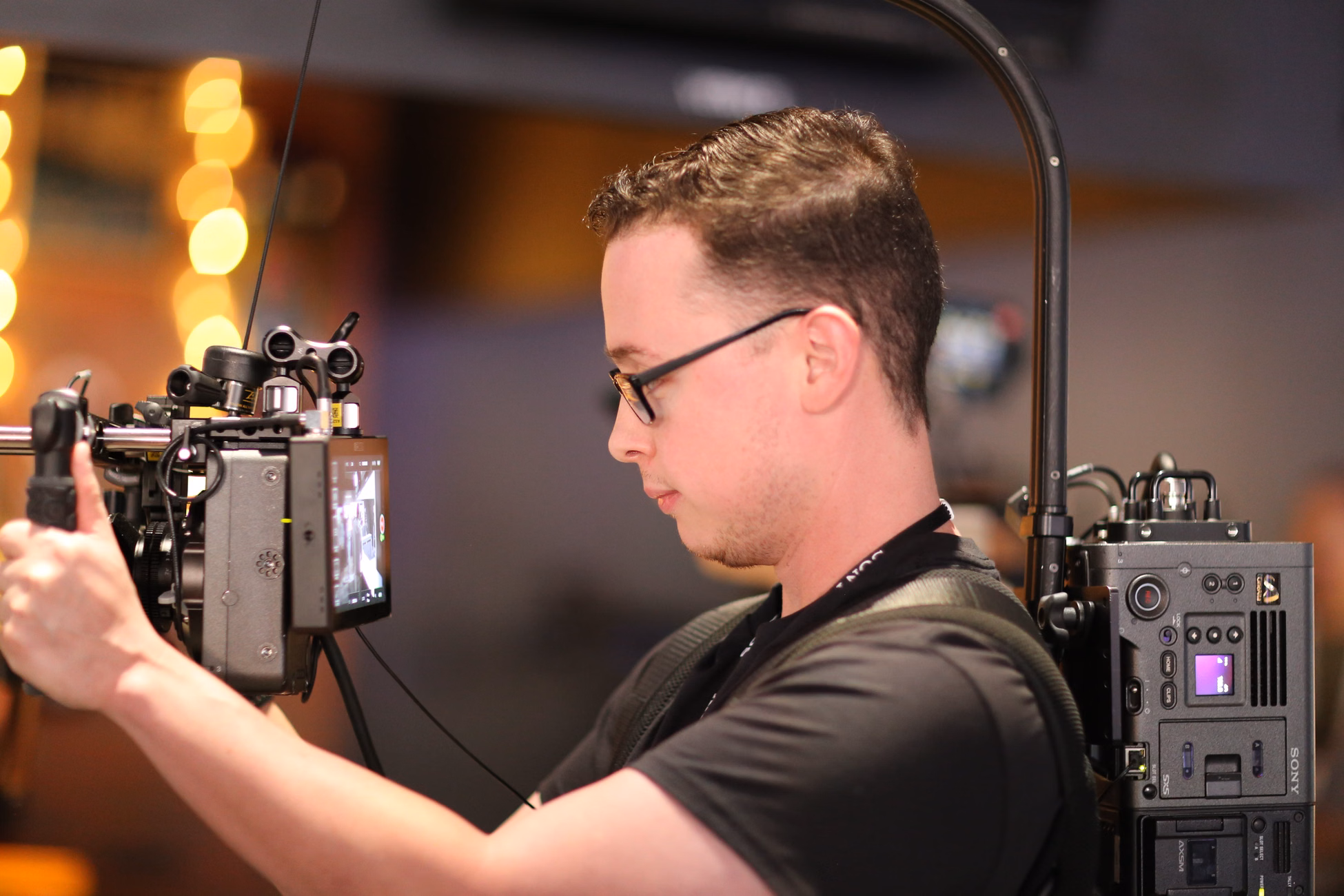 Cameraman operating advanced filming equipment indoors with ambient lighting.