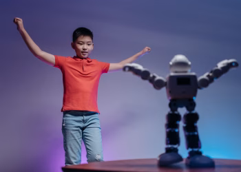 Asian boy in red polo shirt mimicking robot's dance moves under colorful lighting indoors.