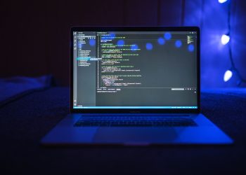 Close-up of a laptop screen displaying code, set against a dark backdrop with blue lighting for a tech-focused ambiance.