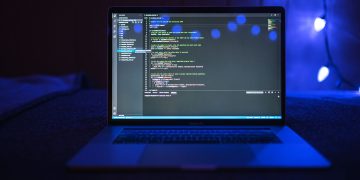 Close-up of a laptop screen displaying code, set against a dark backdrop with blue lighting for a tech-focused ambiance.