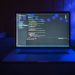 Close-up of a laptop screen displaying code, set against a dark backdrop with blue lighting for a tech-focused ambiance.