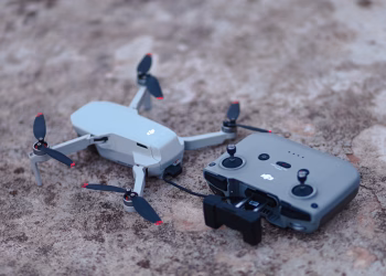 A close-up view of a compact drone and its remote controller on a rough concrete surface.