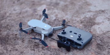 A close-up view of a compact drone and its remote controller on a rough concrete surface.
