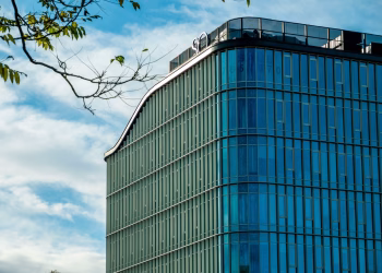 A sleek, modern office building featuring curved glass and metal architecture under a clear blue sky.
