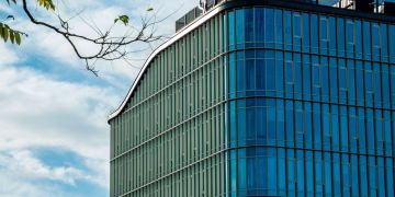 A sleek, modern office building featuring curved glass and metal architecture under a clear blue sky.
