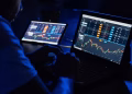 Man analyzing financial charts and data on laptops in a dimly lit room, highlighting forex trading.