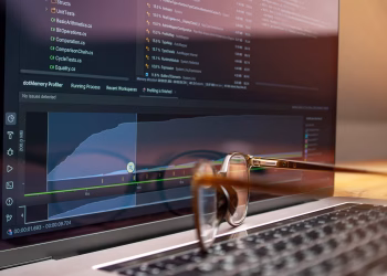 Laptop screen displaying code and performance graphs with eyeglasses resting on the keyboard.