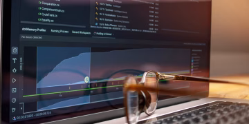 Laptop screen displaying code and performance graphs with eyeglasses resting on the keyboard.