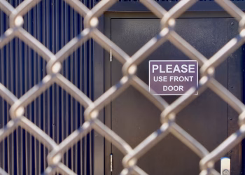 Closeup of a chain-link fence obstructing a door with a 'Please Use Front Door' sign.