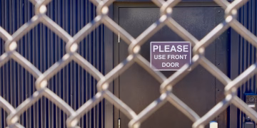 Closeup of a chain-link fence obstructing a door with a 'Please Use Front Door' sign.