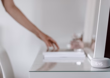 A smart speaker with a digital clock display placed on a minimalist desk setting, hand in background.