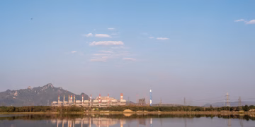 Scenic view of a power plant by a lake, reflecting mountains and a sky with scattered clouds.