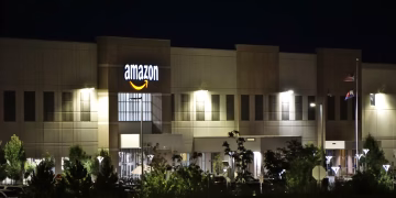 Amazon warehouse building illuminated at night with trees and signage.