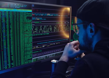 Man intently working on computer programming with code displayed on dual monitors in a dimly lit room.