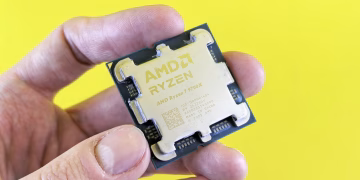 Detailed shot of AMD Ryzen 7 9700X processor held against bright yellow background.