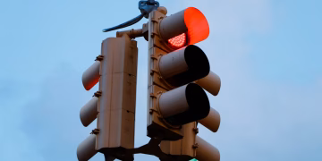 Close-up of a red traffic light signaling stop against a clear blue sky.